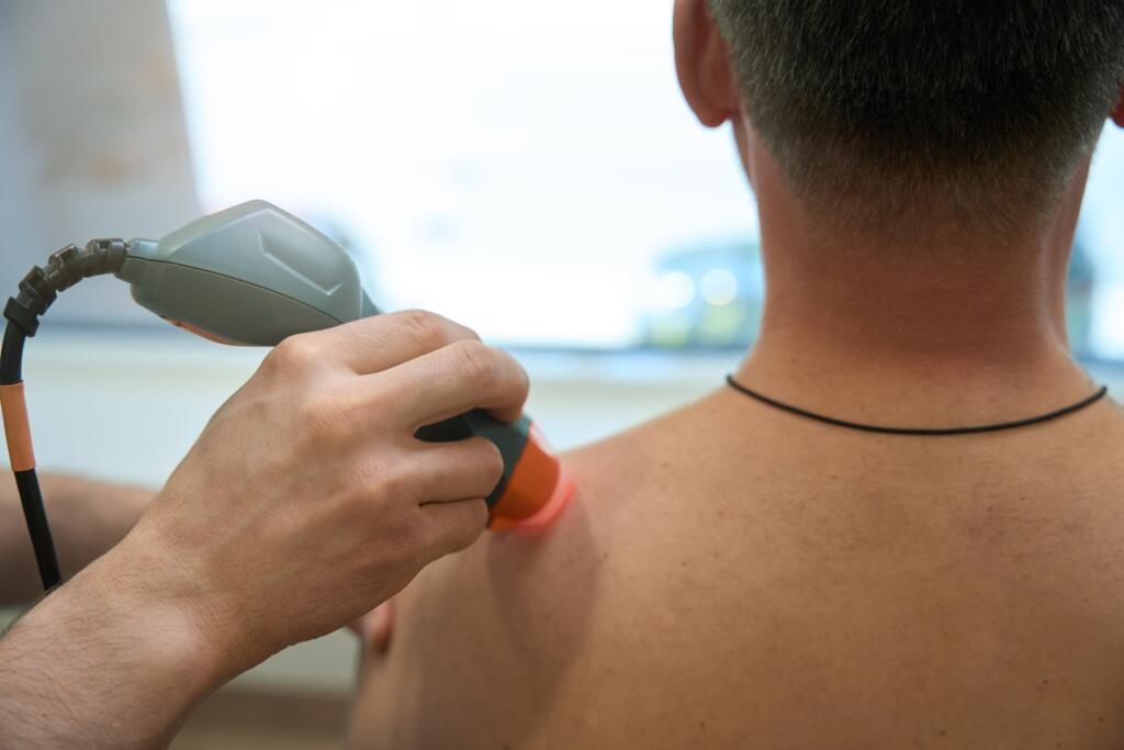 Physician,Treating,Patient,For,Back,Pain,With,Medical,Device - Gardner Physical Therapy Gardner Physical Therapy specialist applying laser therapy to a patient’s shoulder for pain relief and healing.