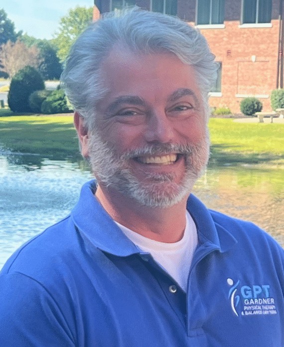 Scott Gardner, founder of Gardner Physical Therapy, smiling in front of a scenic pond outside the clinic.