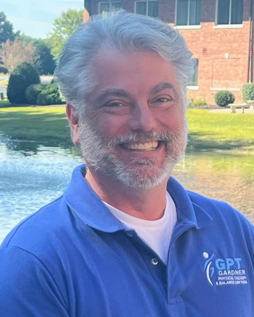 Scott Gardner, founder of Gardner Physical Therapy, smiling in front of a scenic pond outside the clinic.