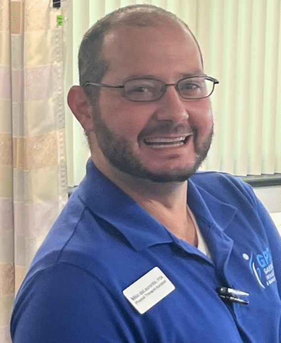 Mike deLaurentis PTA at Gardner Physical Therapy, standing in a treatment room with a friendly smile.