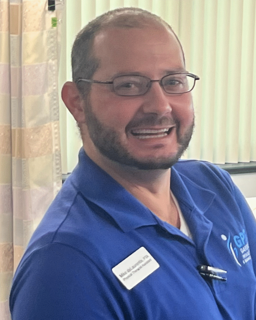 Mike deLaurentis PTA at Gardner Physical Therapy, standing in a treatment room with a friendly smile.