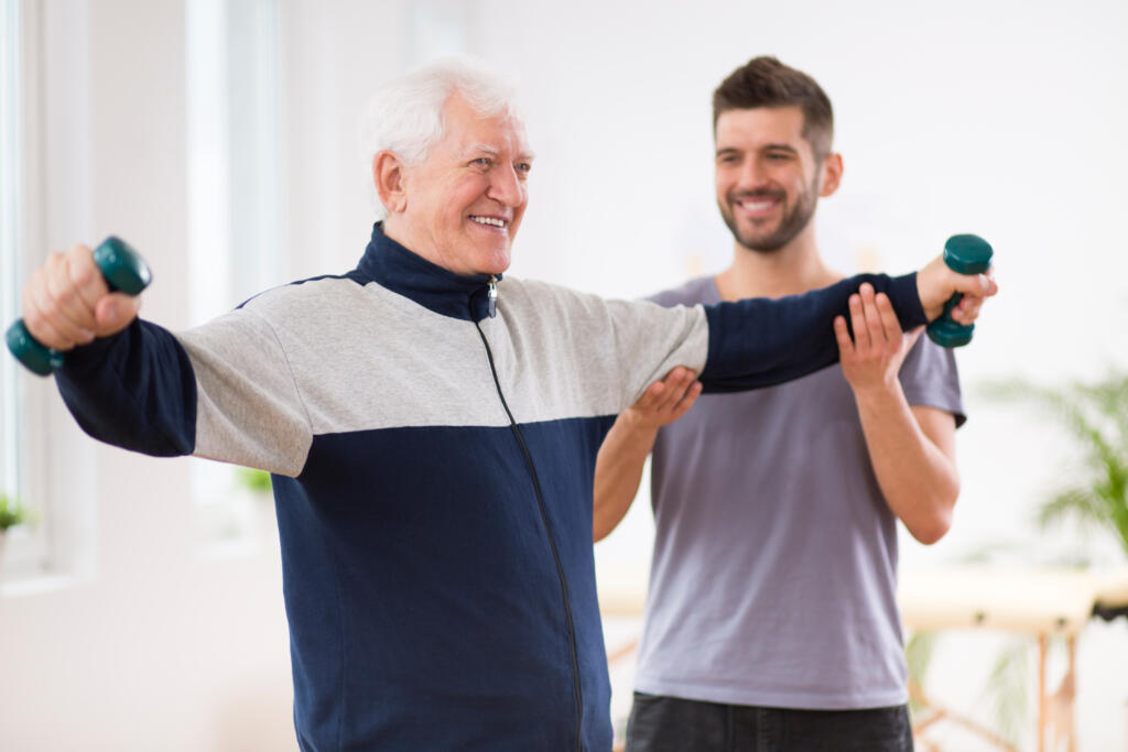 Senior,Man,After,Stroke,At,Nursing,Home,Exercising,With,Professional - Gardner Physical Therapy Senior man exercising with light weights during guided strength and balance training at Gardner Physical Therapy.