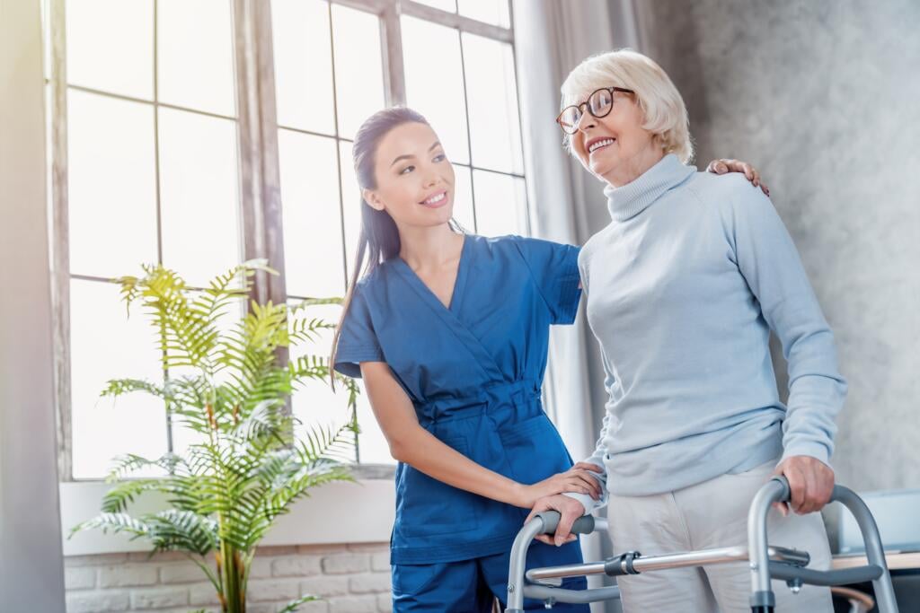 Elderly woman using a walker with the support of a physical therapist during balance training and fall prevention therapy at Gardner Physical Therapy.