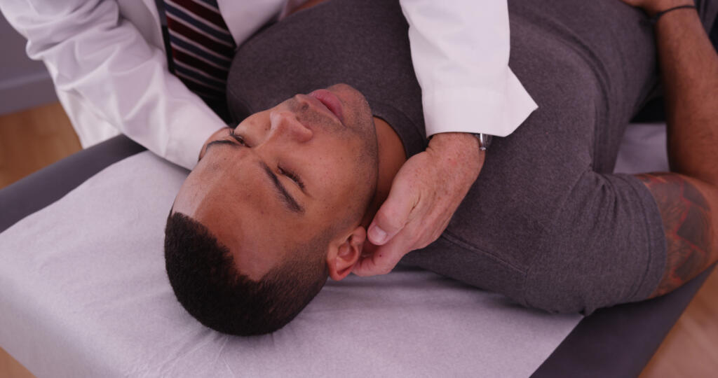 African-american,Male,Patient,Having,Neck,Pain,Examined,By,Chiropractor. - Gardner Physical Therapy Physical therapist providing cervical spine treatment as part of concussion and post-concussion rehabilitation at Gardner Physical Therapy.