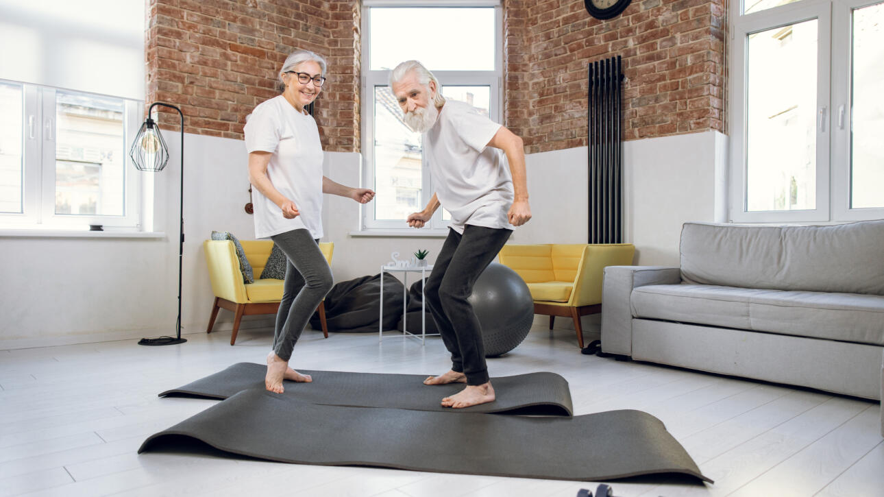 Smiling older couple exercising together on yoga mats in a bright living room for Gardner Physical Therapy.