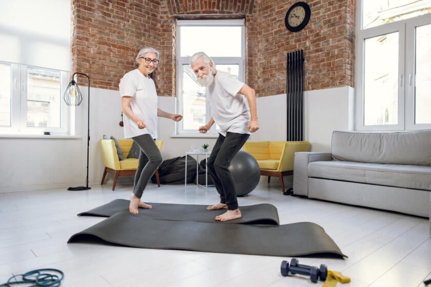 Smiling older couple exercising together on yoga mats in a bright living room for Gardner Physical Therapy.