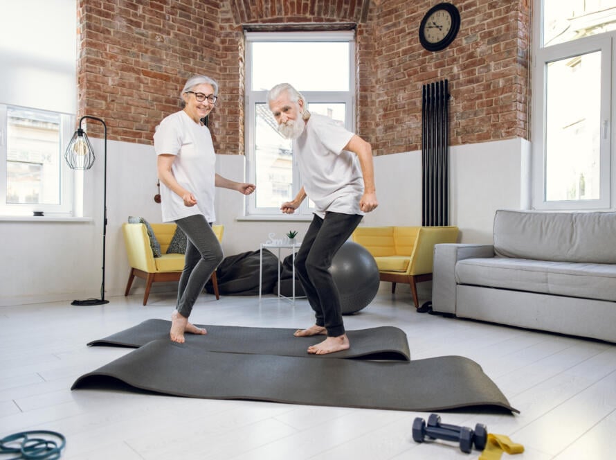 Smiling older couple exercising together on yoga mats in a bright living room for Gardner Physical Therapy.