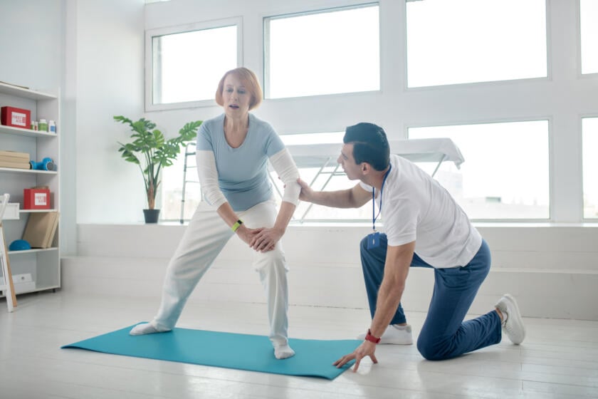 Senior woman stretching on a yoga mat with therapist’s support during Gardner Physical Therapy session.