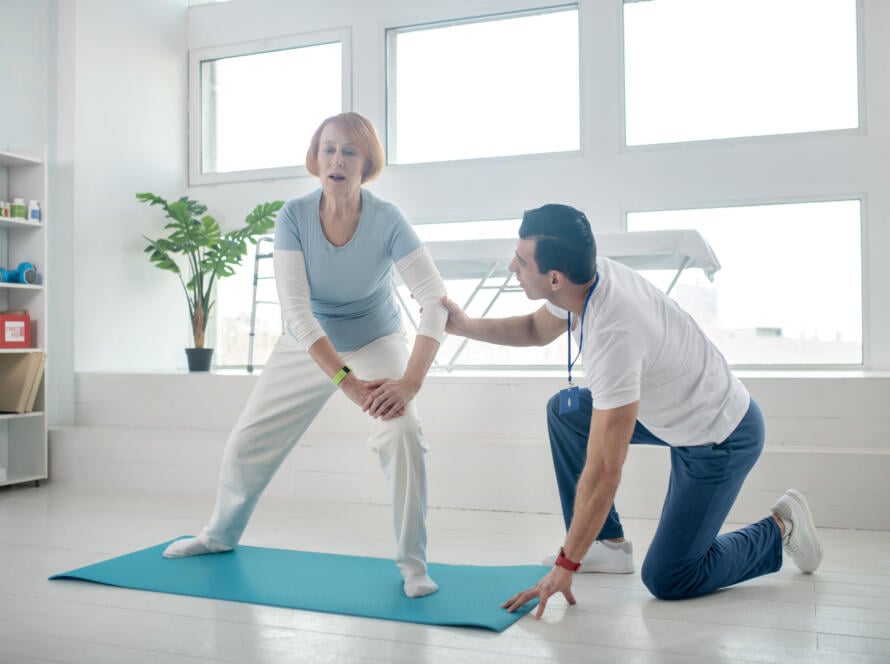Senior woman stretching on a yoga mat with therapist’s support during Gardner Physical Therapy session.