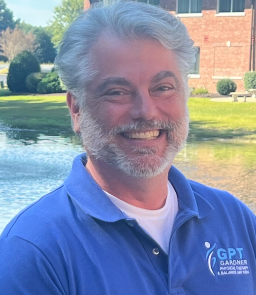 Scott Gardner, founder of Gardner Physical Therapy, smiling in front of a scenic pond outside the clinic.