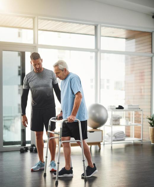 Ocean Pines physical therapist assists senior man walking with a walker during rehabilitation exercise.